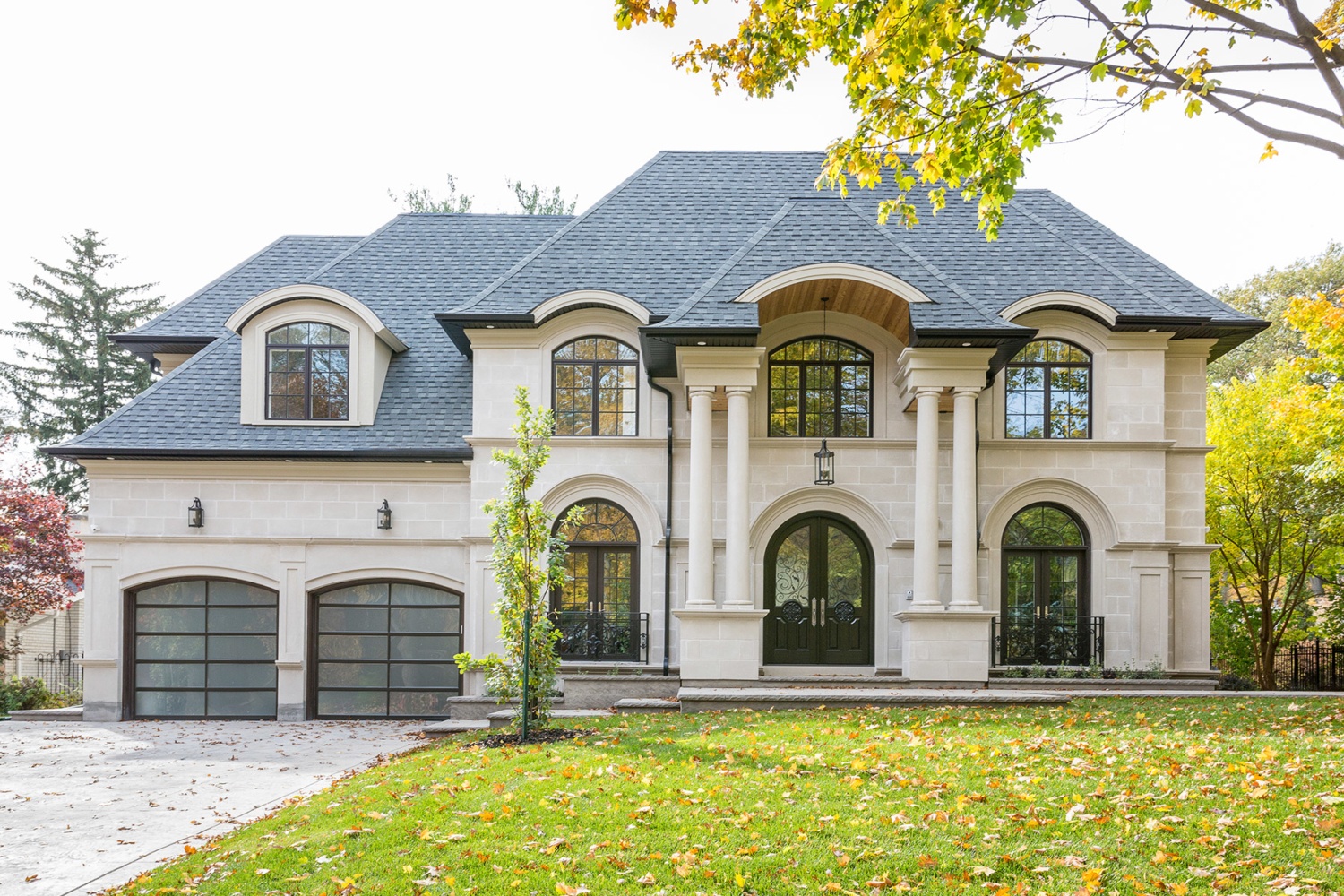 Chateau style home with black trim, light stone and glass garage door.