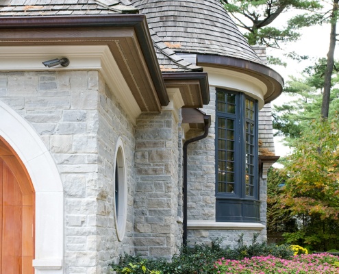 Traditional home design with wood garage door, stone siding and wood detailing.