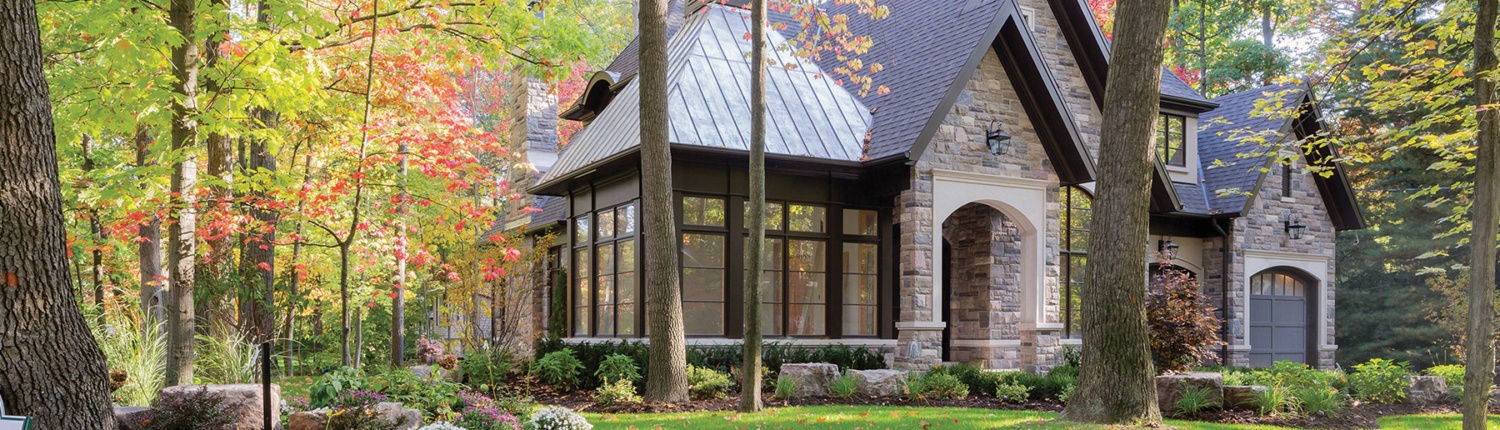 Traditional home design with natural stone, dark brown trim and large windows.