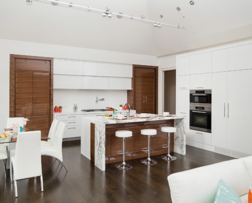 Modern kitchen with double oven, wood cabinets and white barstool.