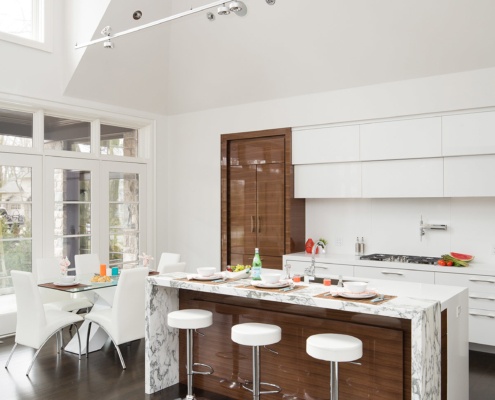 Open concept kitchen with marble island, white cabinets and track lighting.