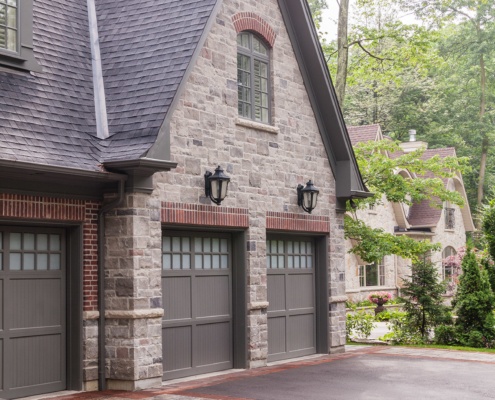 Custom home design with gray garage door, arched window and brick accents.