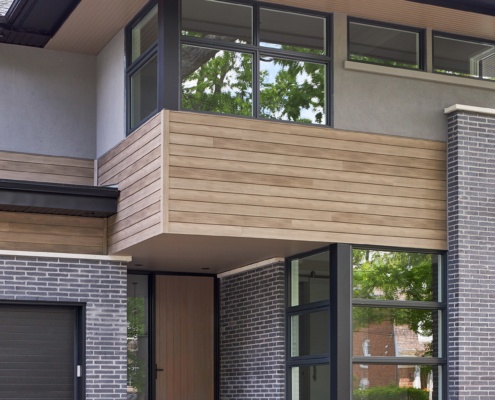 Contemporary house with wood front door, wood siding and floor to ceiling window.