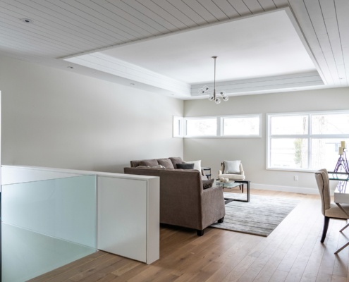 Modern sitting area with wood ceiling, modern chandelier and glass railing.