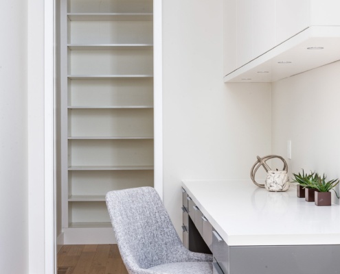 Modern kitchen pantry with white trim, built in desk and hardwood floor.