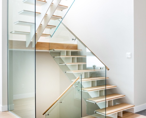 Floating stair with light wood treads, glass railing and white baseboard.