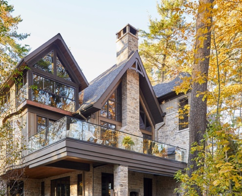 Stone house with glass railing, stone chimney and covered porch.