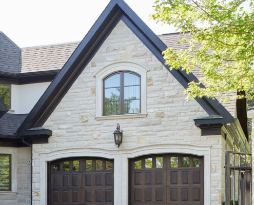 Toronto house with wood garage door, stone siding and arched window.
