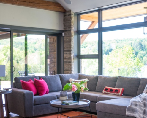 Modern family room with floor to ceiling windows, gray couch and wood beam.