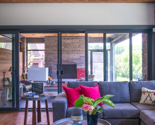 Family room with wood beam, gray couch and black frame windows.