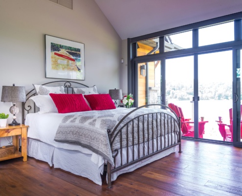 Cottage master bedroom with floor to ceiling windows, hardwood floor and black trim.
