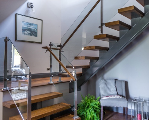 Rustic floating staircase with glass railing, dark baseboard and hardwood floor.