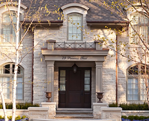 Chateau architecture with natural stone, wood garage door and stucco columns.