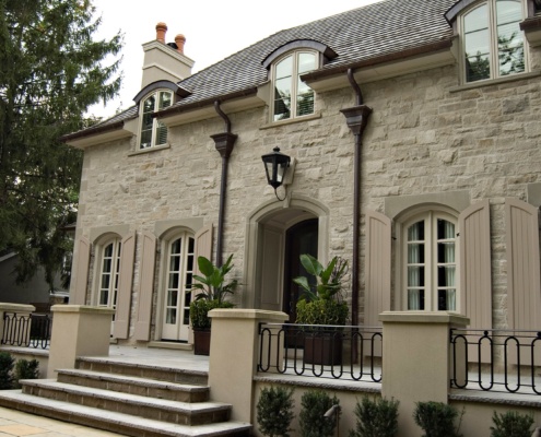 Chateau style home with arched window, stucco chimney and stone terrace.