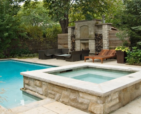 Home backyard with inground pool, stone deck and outdoor fireplace.