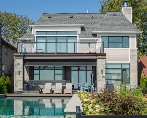 Transitional home exterior with wood siding, outdoor kitchen and large windows.