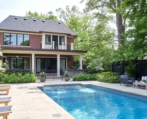 Custom house backyard with inground pool, stone patio and black frame windows.