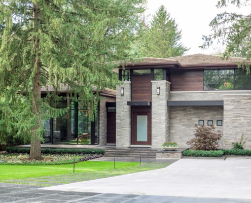 Contemporary home with shingled roof, concrete driveway and wood front door.