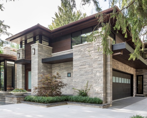 Modern home with wood garage door, natural stone and floating roof.