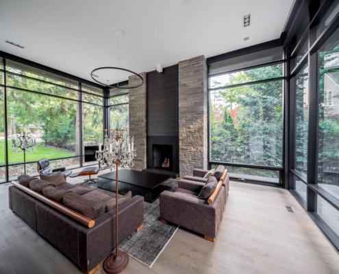 Living room with stone fireplace, modern chandelier and large windows.