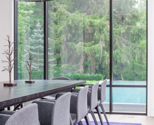 Glass dining room with black frame windows, hardwood floor and wood dining table.