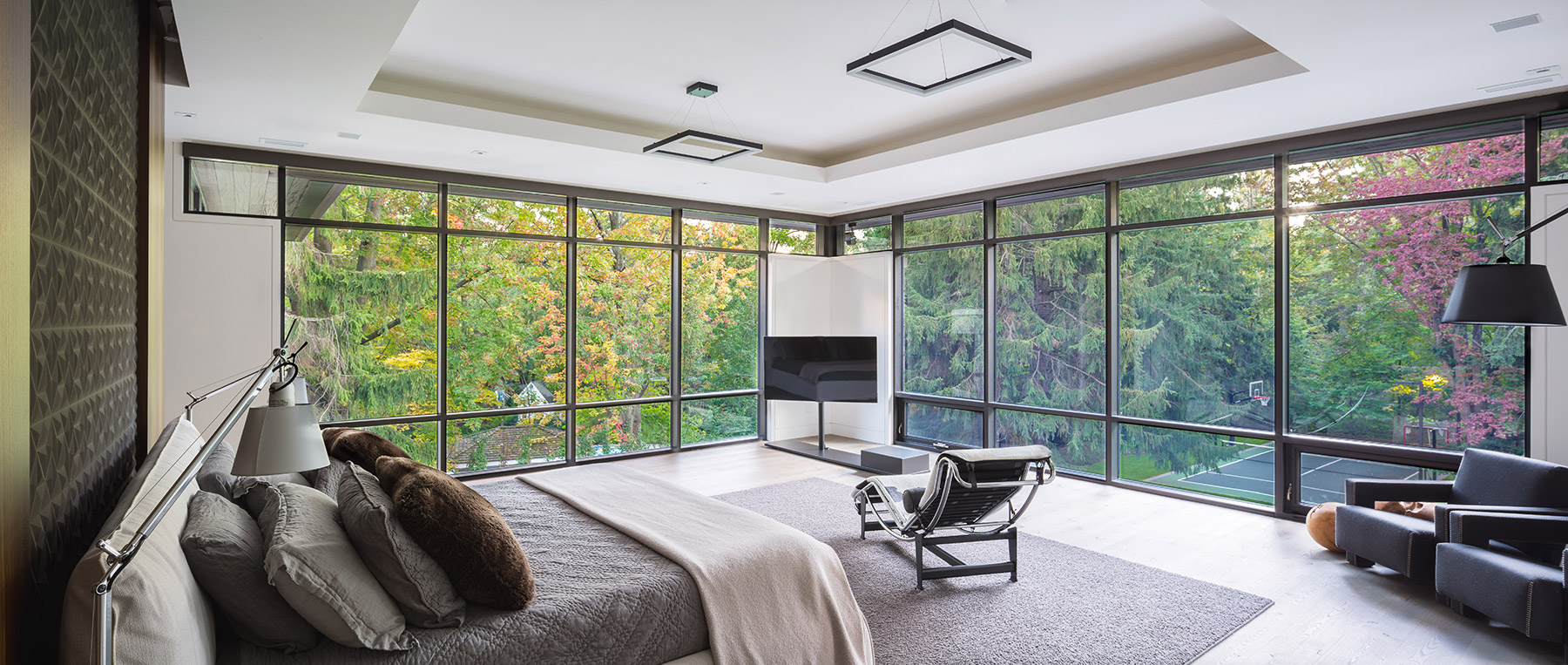 Modern master bedroom with floor to ceiling windows, recessed ceiling and hardwood flooring.