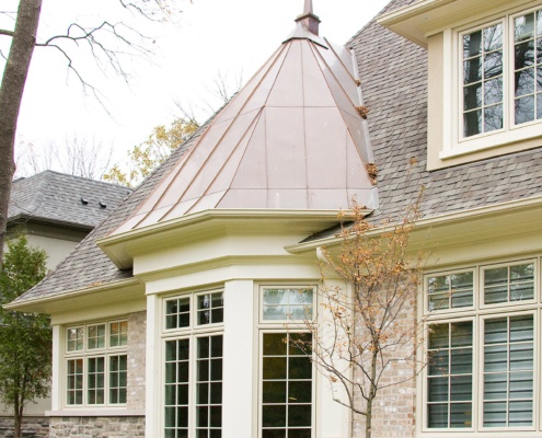 Traditional home with stone siding, white frame windows and copper roof.