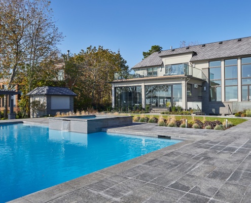 Home rear exterior with stucco siding, horizontal stone and inground pool.