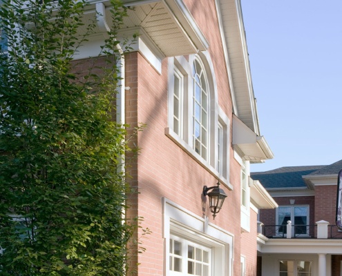 Custom home exterior with white grage door, white frame windows and bricks siding.