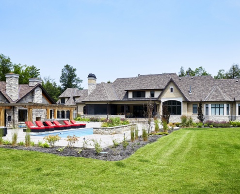 Milton home with stone patio, inground pool and shingled roof.