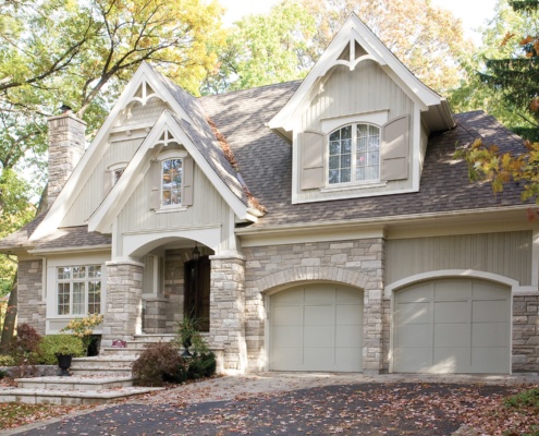 Custom home with stone skirt, arched garage doors and vertical siding.