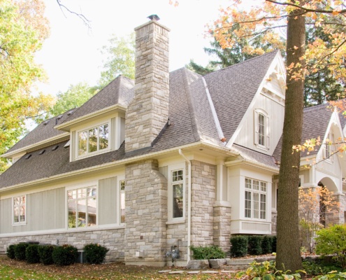 Traditional house with stone chimney, white frame windows and wood siding.