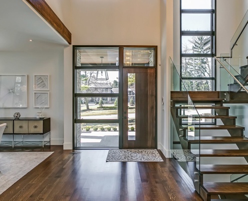 Home front entry with wood front door, black frame windows and wood beam.