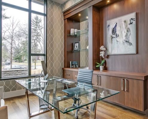 Home office with wood cabinets, wallpaper and white baseboard.