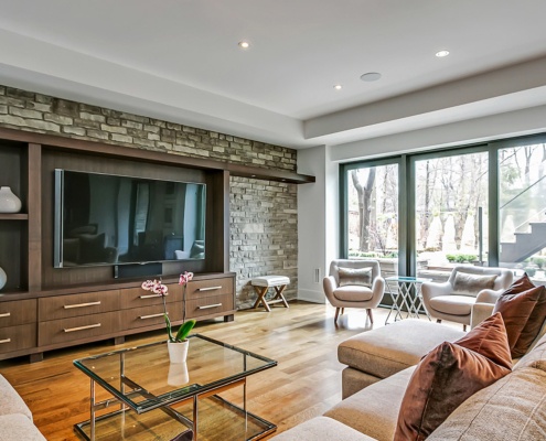 Family room with stone wall, built in cabinets and hardwood floor.