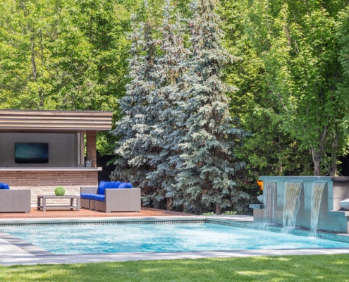 Wood deck with inground pool, outdoor bar and waterfall feature.