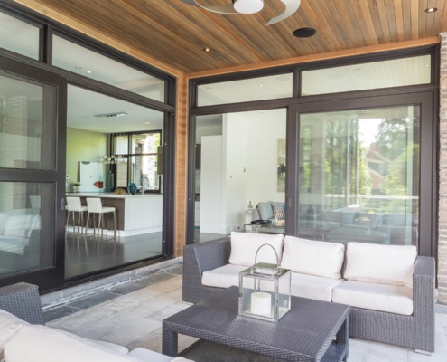 Covered stone patio with wood ceiling, black frame windows and stone wall.