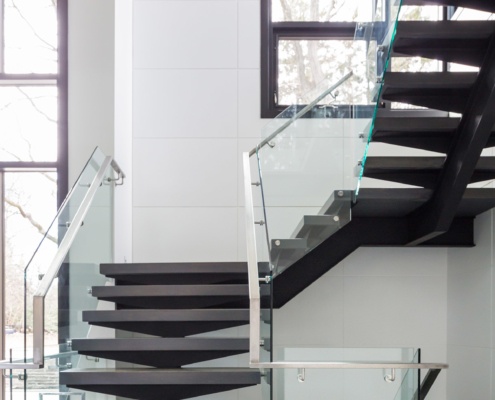 Floating staircase with wood treads, glass railing and black frame window.