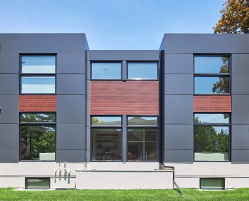 Modern house with flat roof, black siding and floor to ceiling windows.