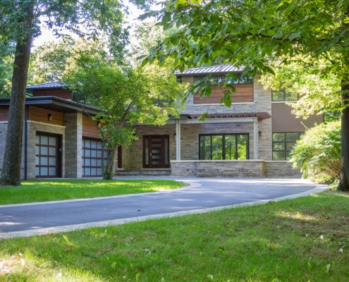 Natural modern with metal roof, black frame windows and glass garage doors.