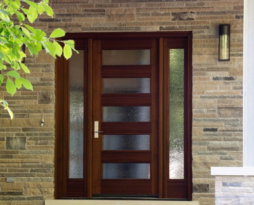Modern front entry with wood front door, stone steps and horizontal stone wall.