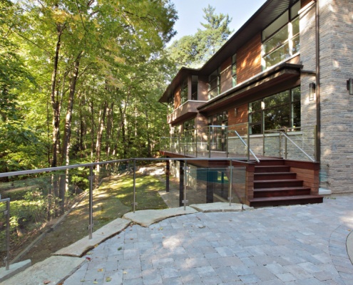 Home wood deck with glass railing and stone patio.