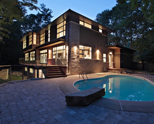 Home rear exterior with stone patio, inground pool and horizontal stone.