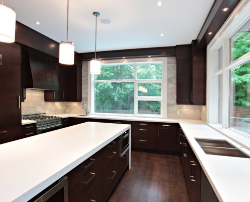 Wood kitchen with white countertops, large windows and tile backsplash.