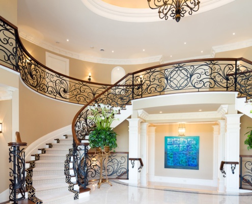 Spiral staircase with metal railing, chandelier and white columns.