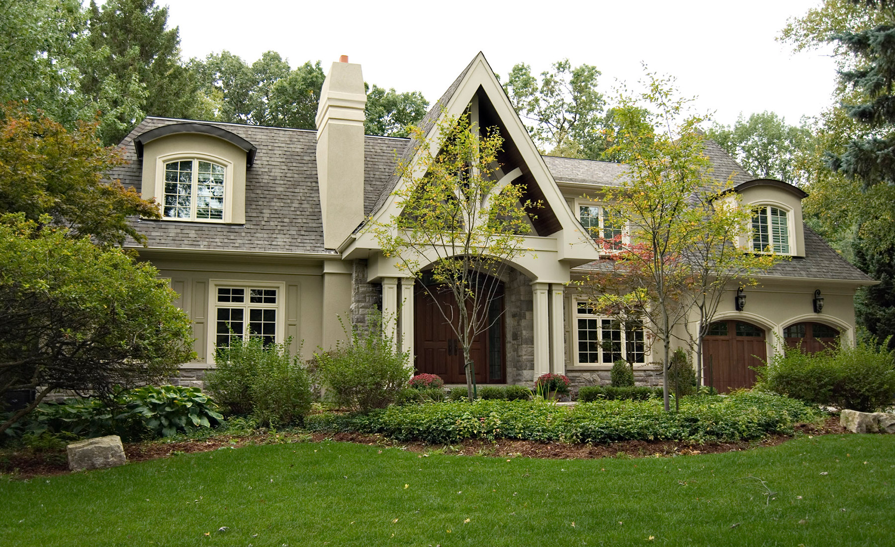 Traditional house with stucco chimney, white frame windows and wood garage doors.