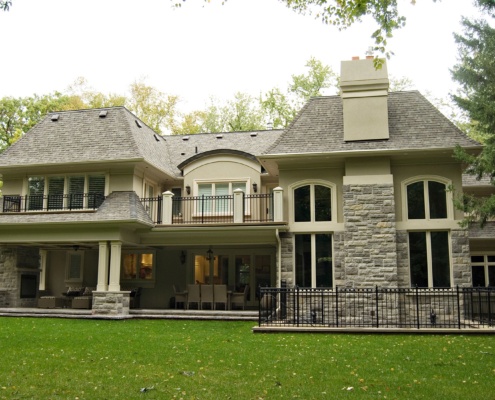 Rear home exterior with second floor balcony, stone chimney and stucco siding.