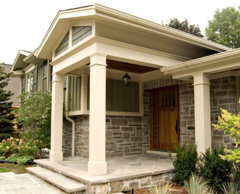 Home front entry with white columns, wood siding and wood soffit.
