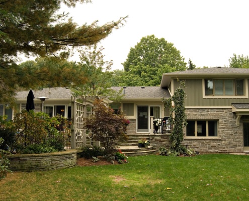 Rear yard with green wood siding, natural stone and shingled roof.