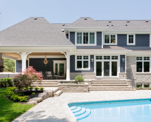 Gray house with white frame windows, stone chimney and stone patio.